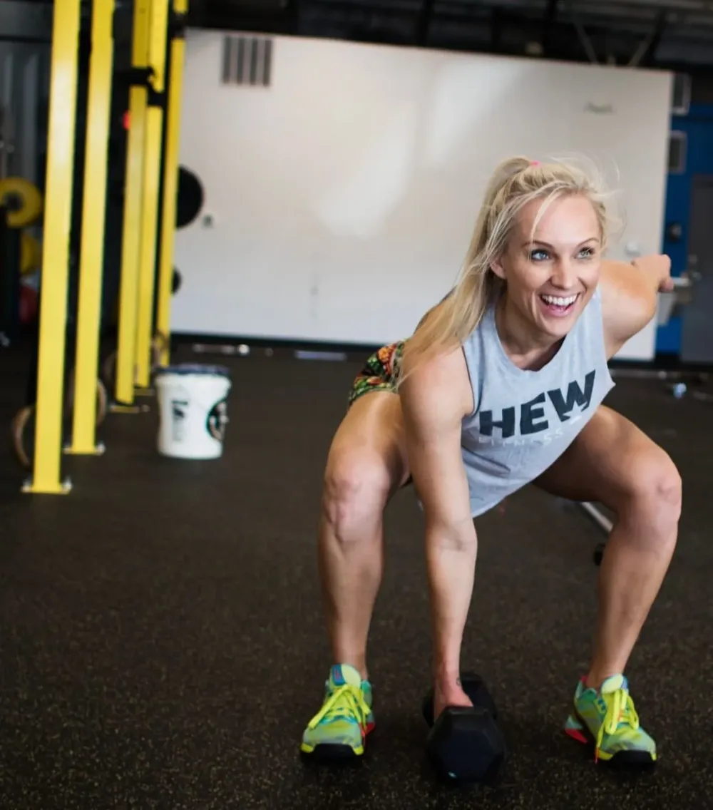 A smiling HEW member mid dumbbell snatch on the gym floor